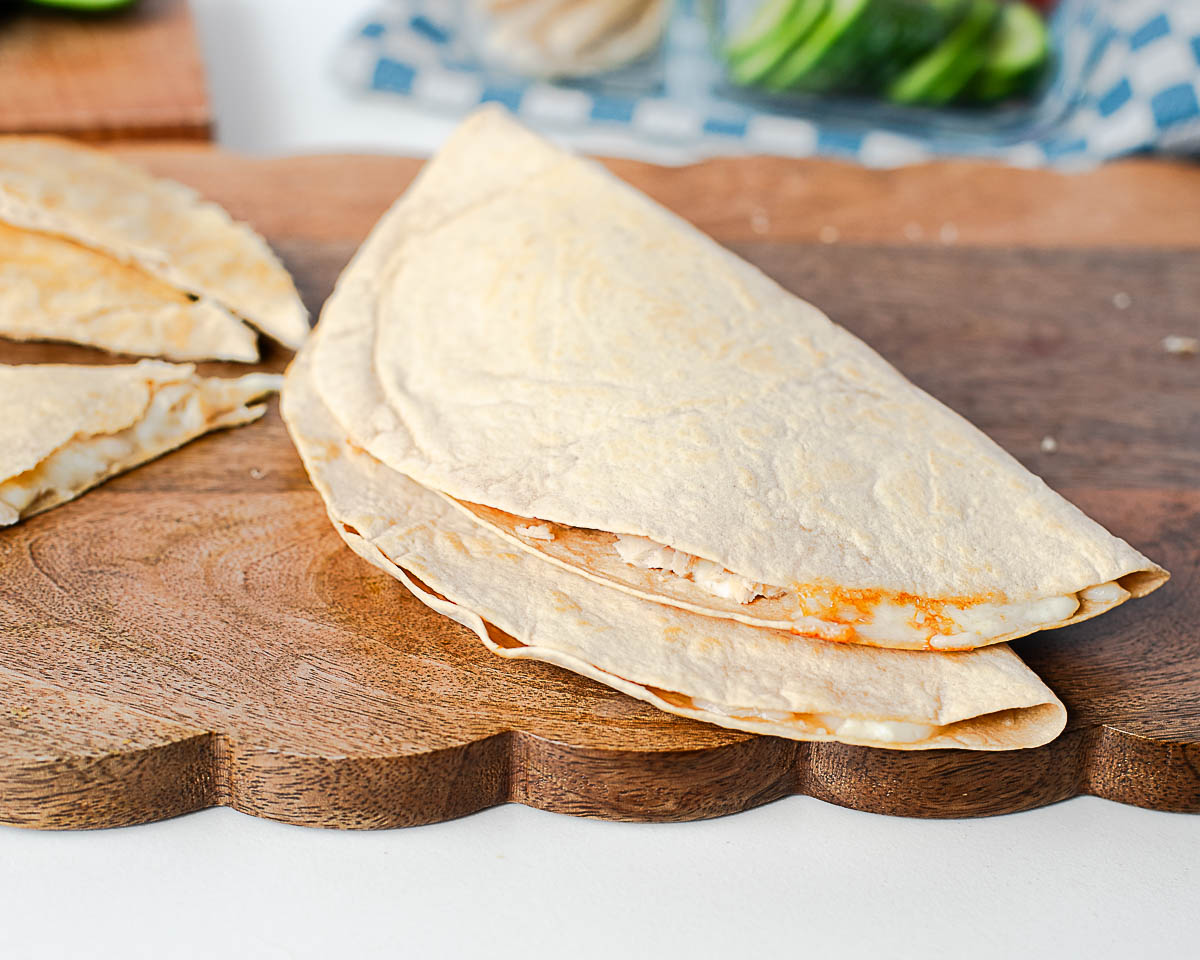 Close-up of folded tuna melt quesadillas stacked on a wooden board, showing melted cheese inside.