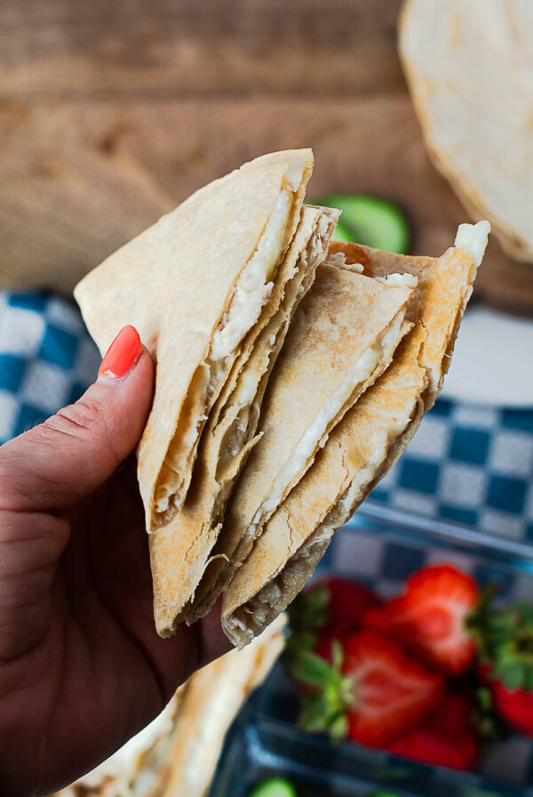 Hand holding a triangular tuna melt quesadilla wedge, showing the melty cheese and tuna filling inside.