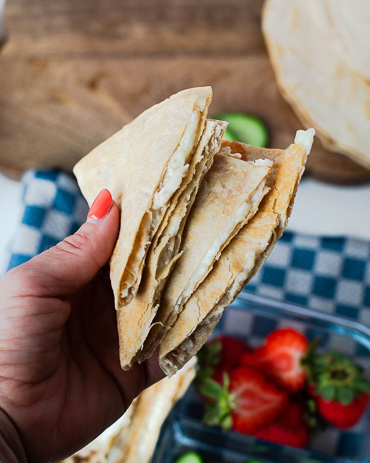 Hand holding a triangular tuna melt quesadilla wedge, showing the melty cheese and tuna filling inside.