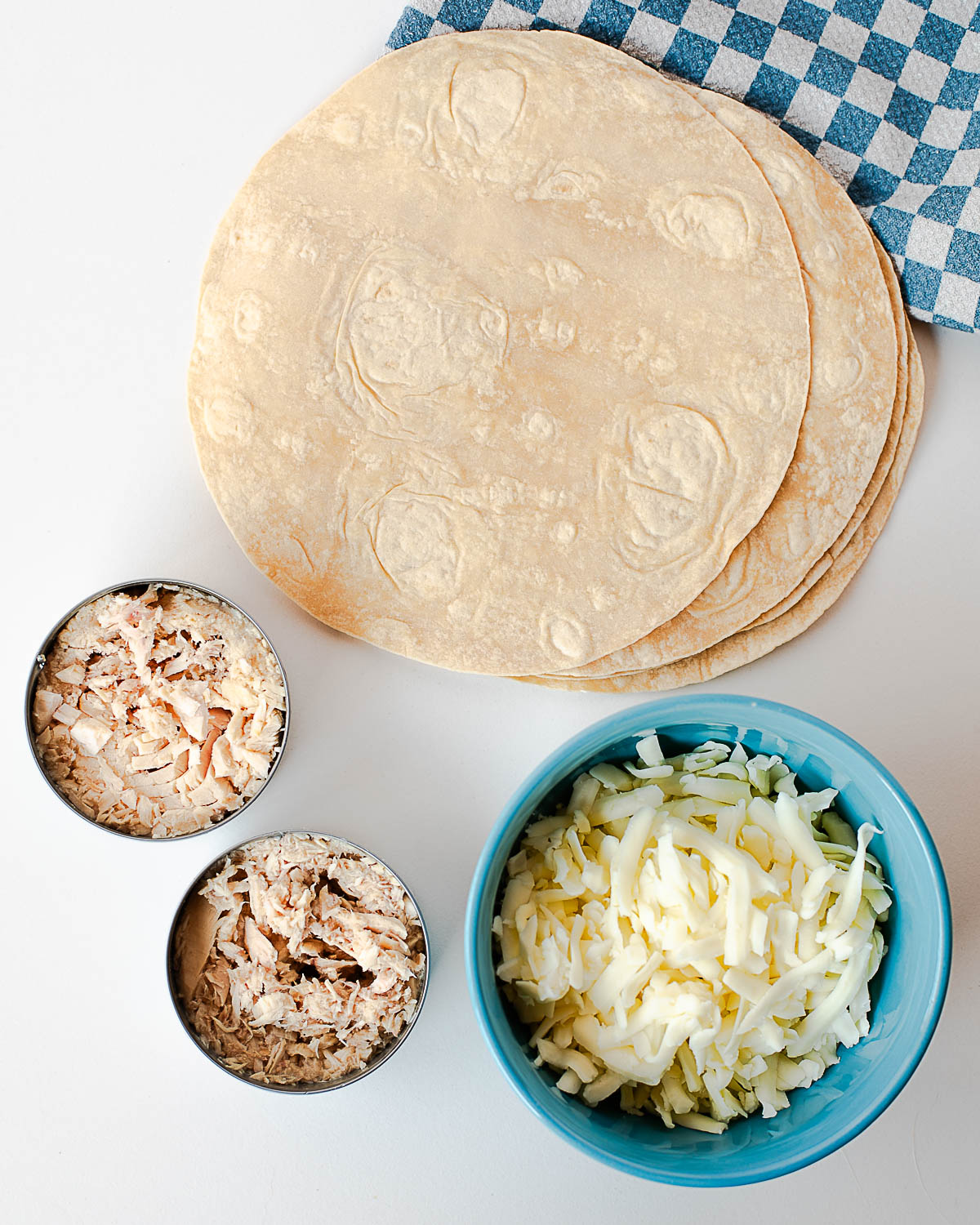 Ingredients for tuna melt quesadillas including flour tortillas, drained canned tuna, and shredded mozzarella cheese.