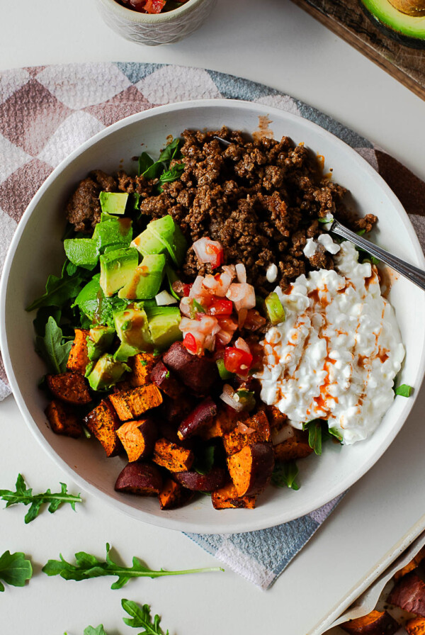 Balanced taco bowl meal with arugula, taco seasoned beef, sweet potatoes, cottage cheese and fresh salsa