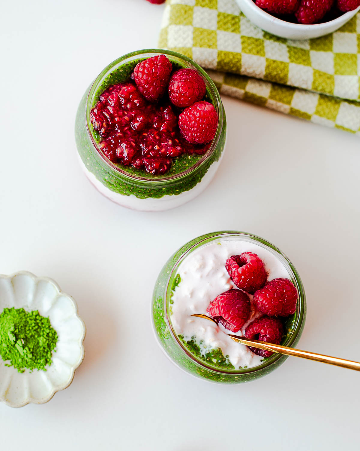 Raspberry overnight oats parfaits layered with matcha chia pudding, creamy yogurt, and mashed raspberries in glass jars.