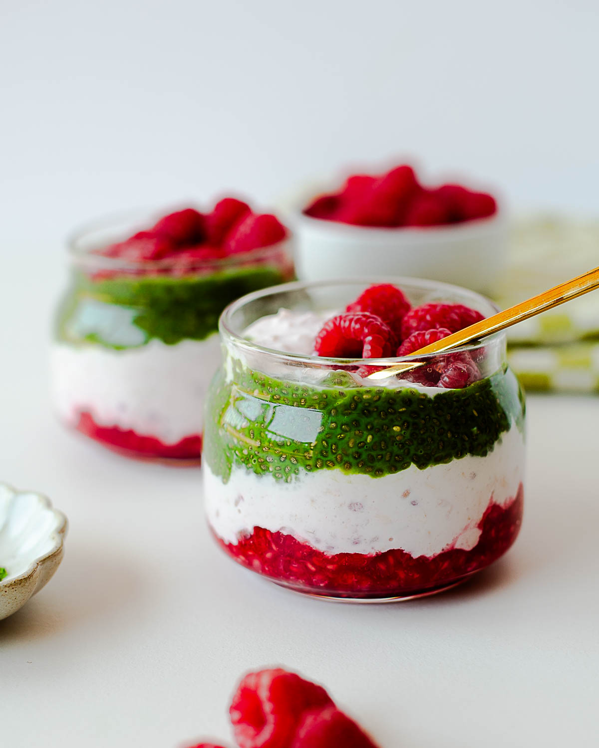 Stunning raspberry overnight oats and matcha chia pudding parfait showing distinct green, white, and red layers.