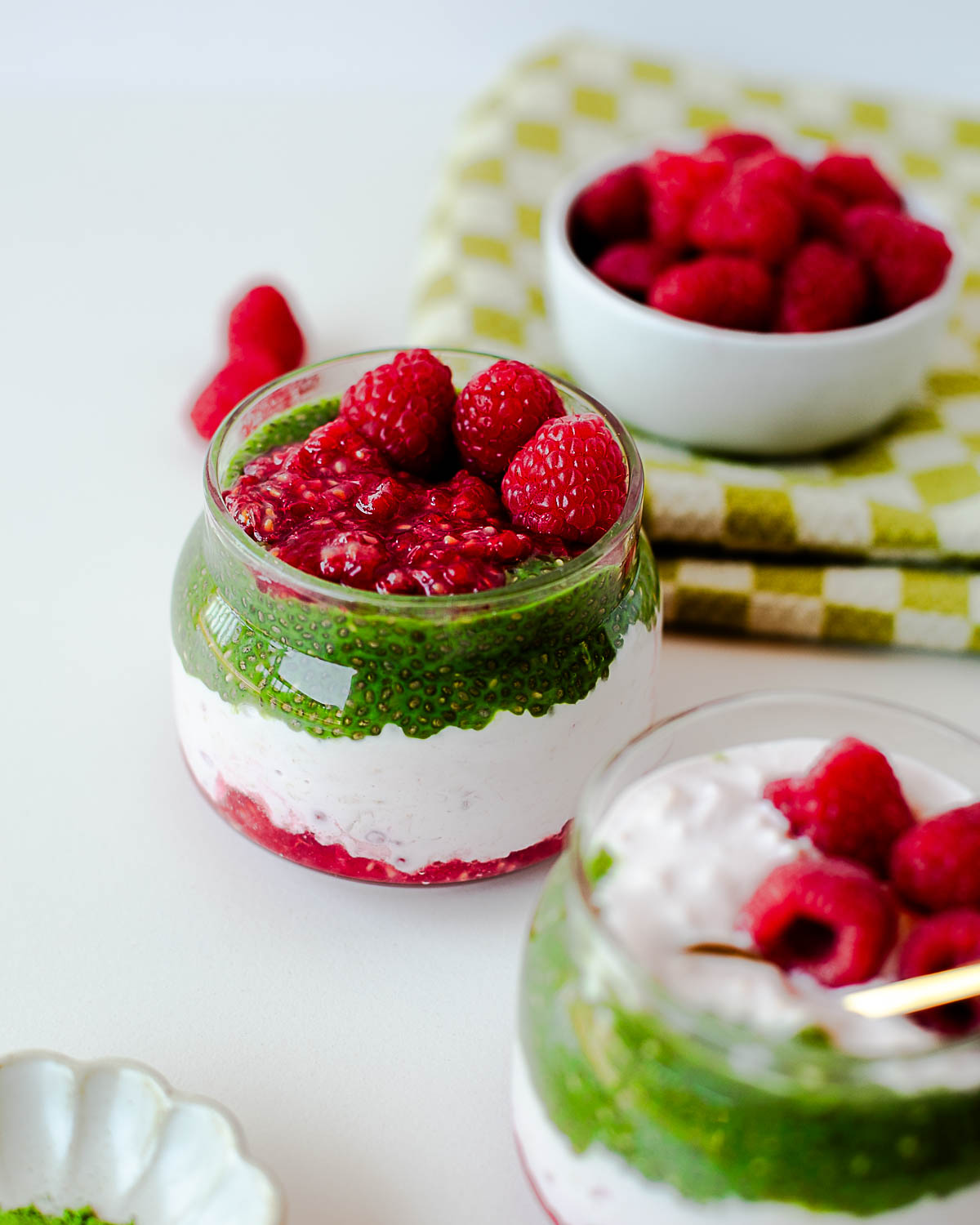 Raspberry overnight oats parfait topped with mashed raspberries and fresh berries, layered with matcha chia pudding.