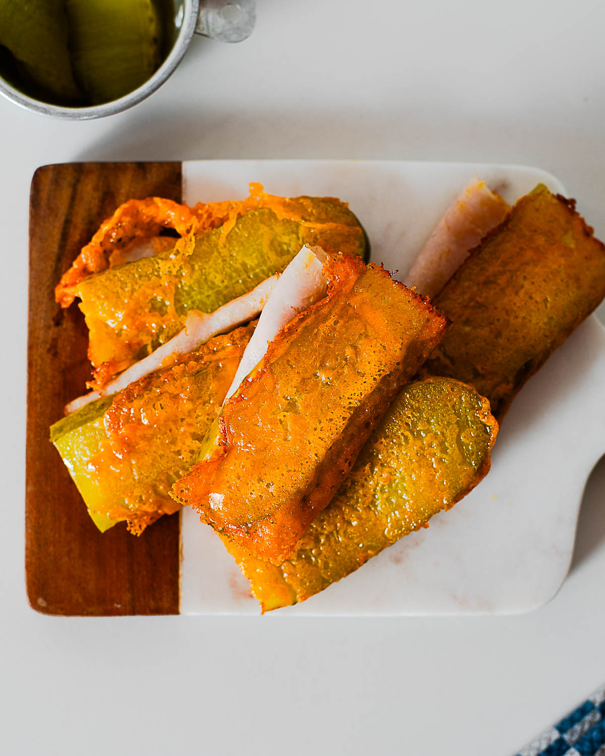 Crispy cheese-wrapped pickle chickles with deli turkey slices on a marble and wood serving board