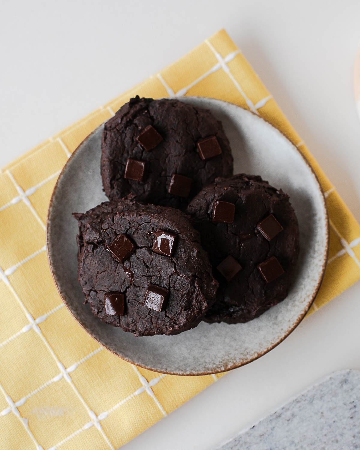 Plate of baked black bean cookies with chocolate chunks on a yellow cloth