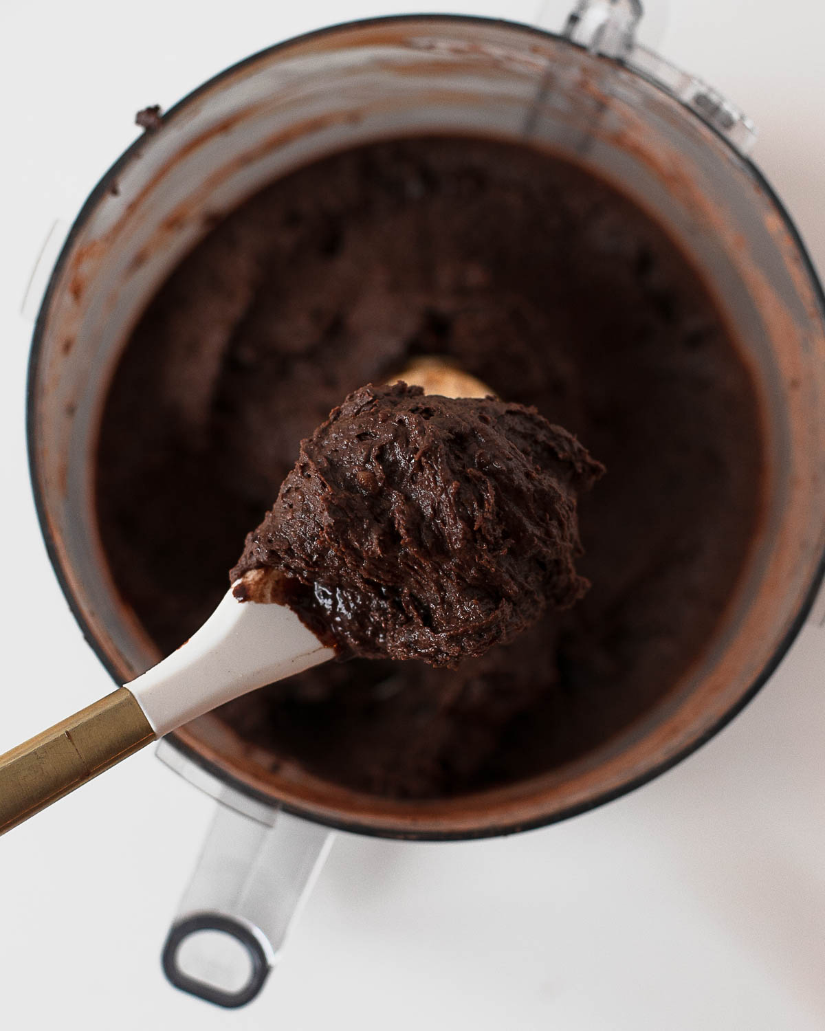 Thick chocolate cookie dough made from black beans in a food processor on a spoon