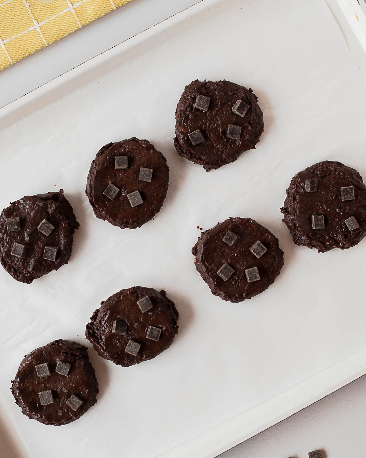 Scooped black bean cookie dough portions on parchment-lined baking sheet with chocolate chunks