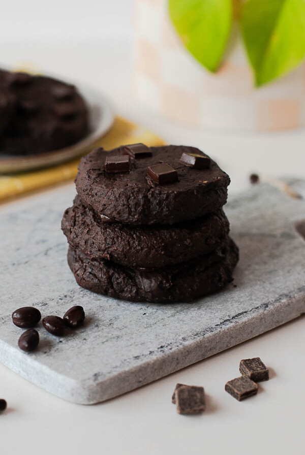 Stack of fudgy chocolate black bean cookies on a stone board with chocolate pieces