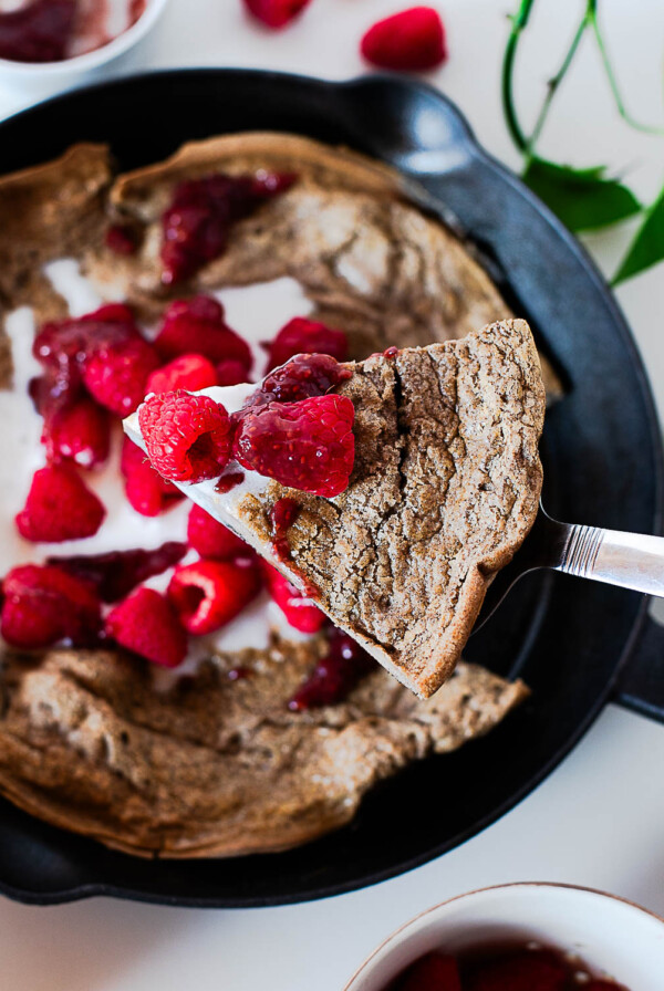 Buckwheat dutch baby in a cast iron skillet topped with whipped cream and fresh raspberries