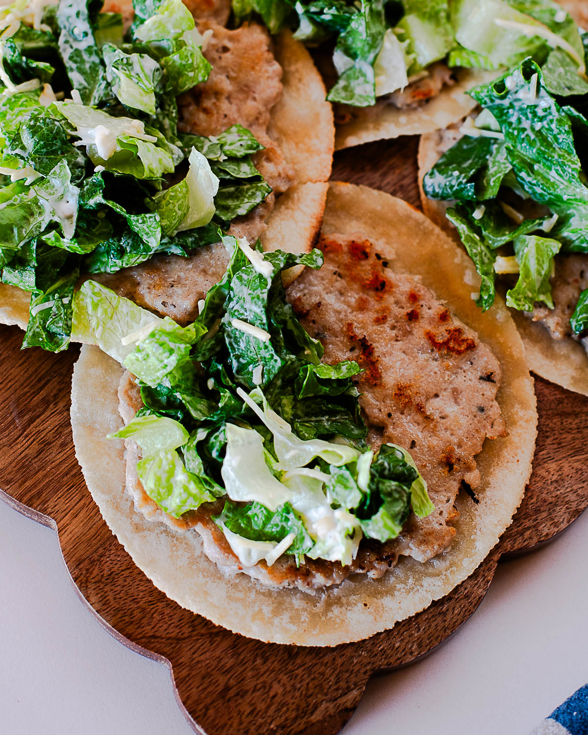 Chicken caesar smash tacos stacked on a plate with romaine caesar salad topping.