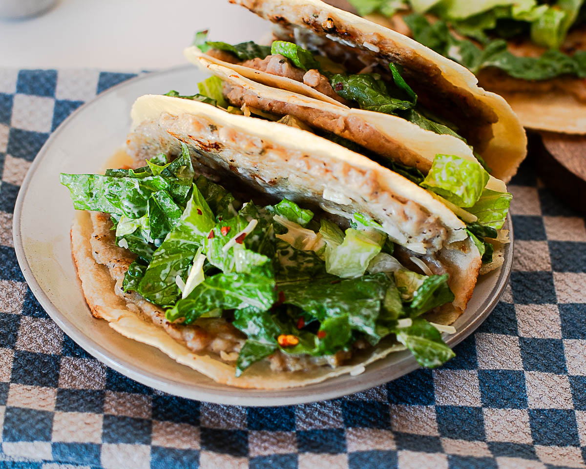 Side view of crispy tortilla chicken caesar smash taco filled with seasoned ground chicken and romaine.