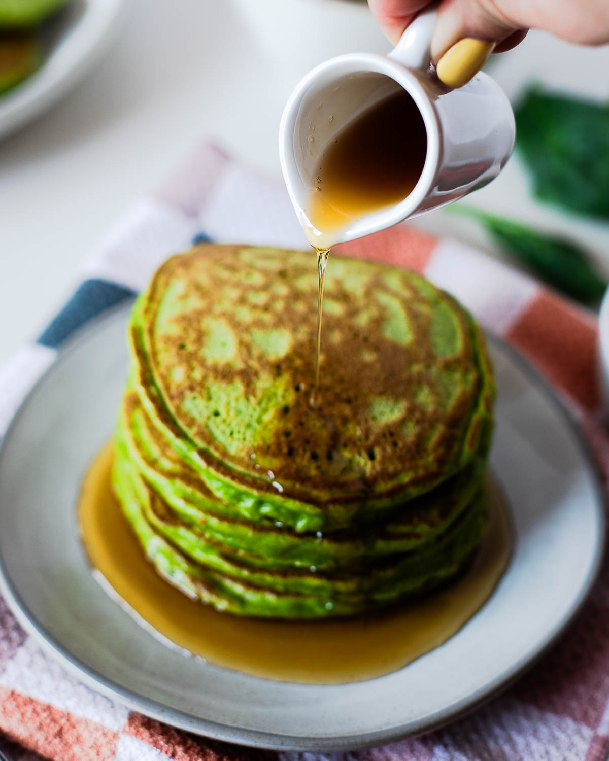 Maple syrup being poured over a stack of green einkorn pancakes