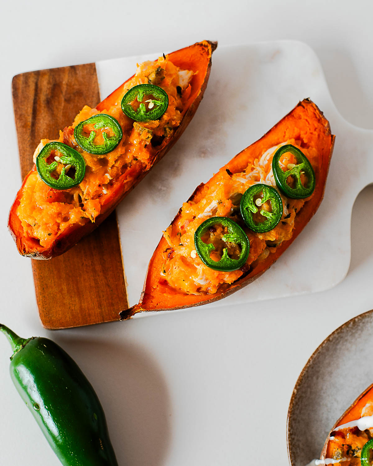 Two loaded jalapeño popper sweet potato halves on cutting board