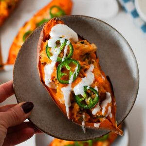 High protein twice baked jalapeño popper sweet potatoes topped with melted cheddar, shredded chicken, crispy bacon, and fresh jalapeño slices on a plate