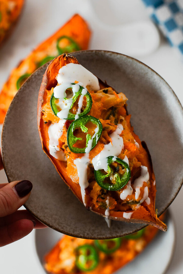 High protein twice baked jalapeño popper sweet potatoes topped with melted cheddar, shredded chicken, crispy bacon, and fresh jalapeño slices on a plate