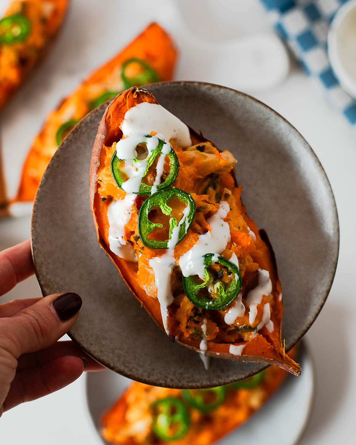 High protein twice baked jalapeño popper sweet potatoes topped with melted cheddar, shredded chicken, crispy bacon, and fresh jalapeño slices on a plate