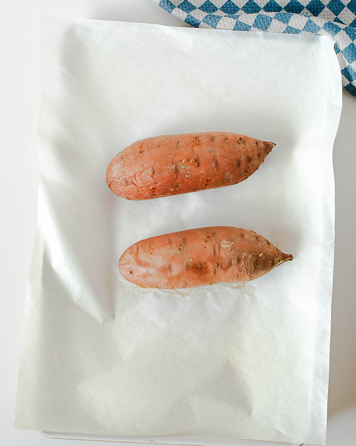 Raw sweet potatoes on parchment-lined baking sheet