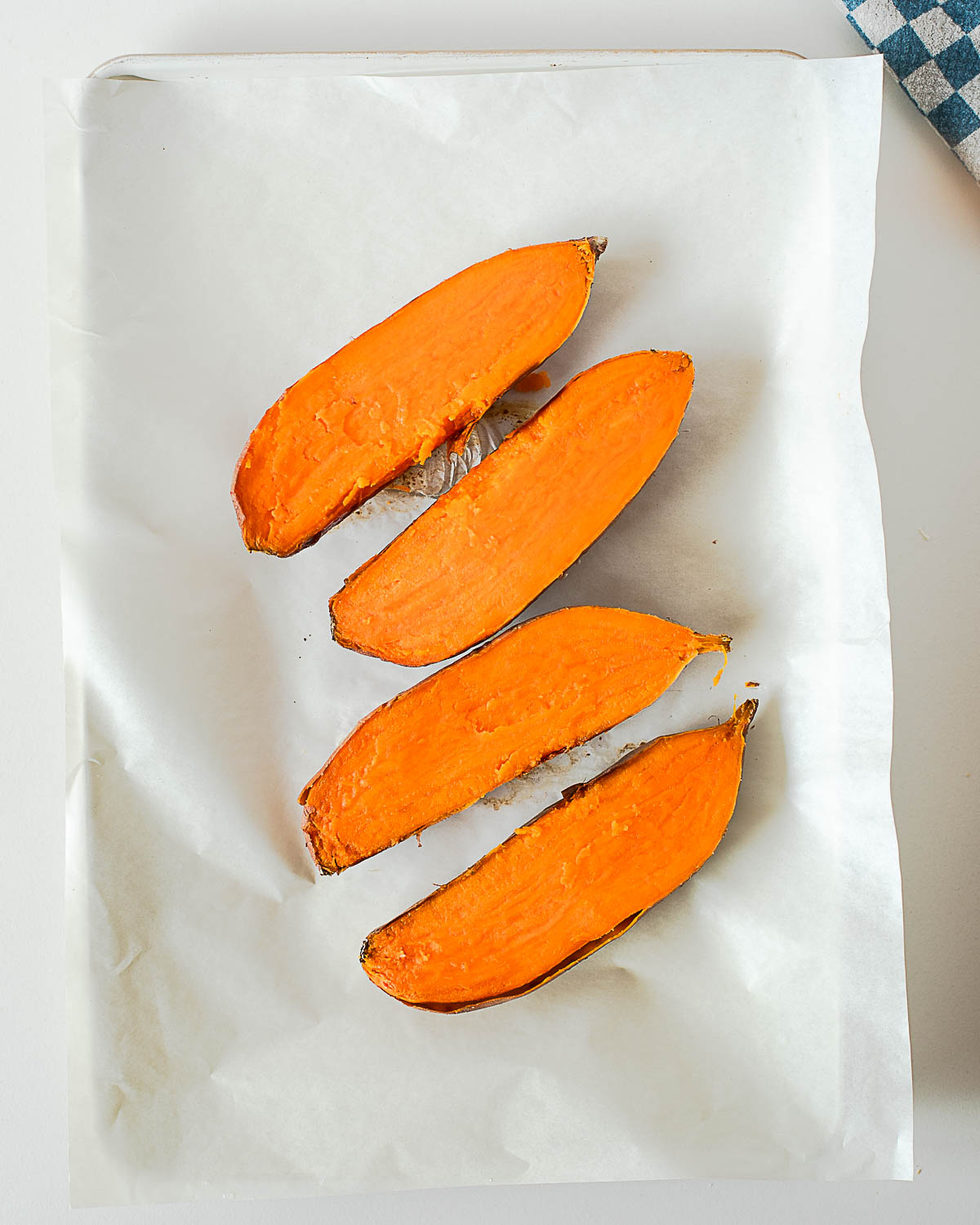 Baked sweet potatoes sliced in half on baking sheet