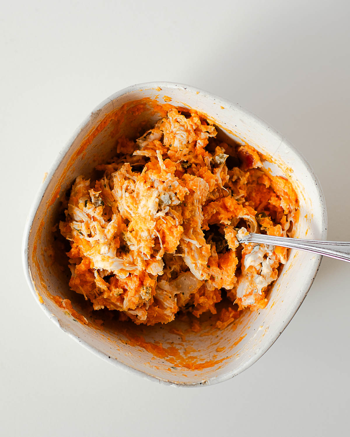 Mashed sweet potato mixed with shredded chicken, bacon, and cheese in bowl