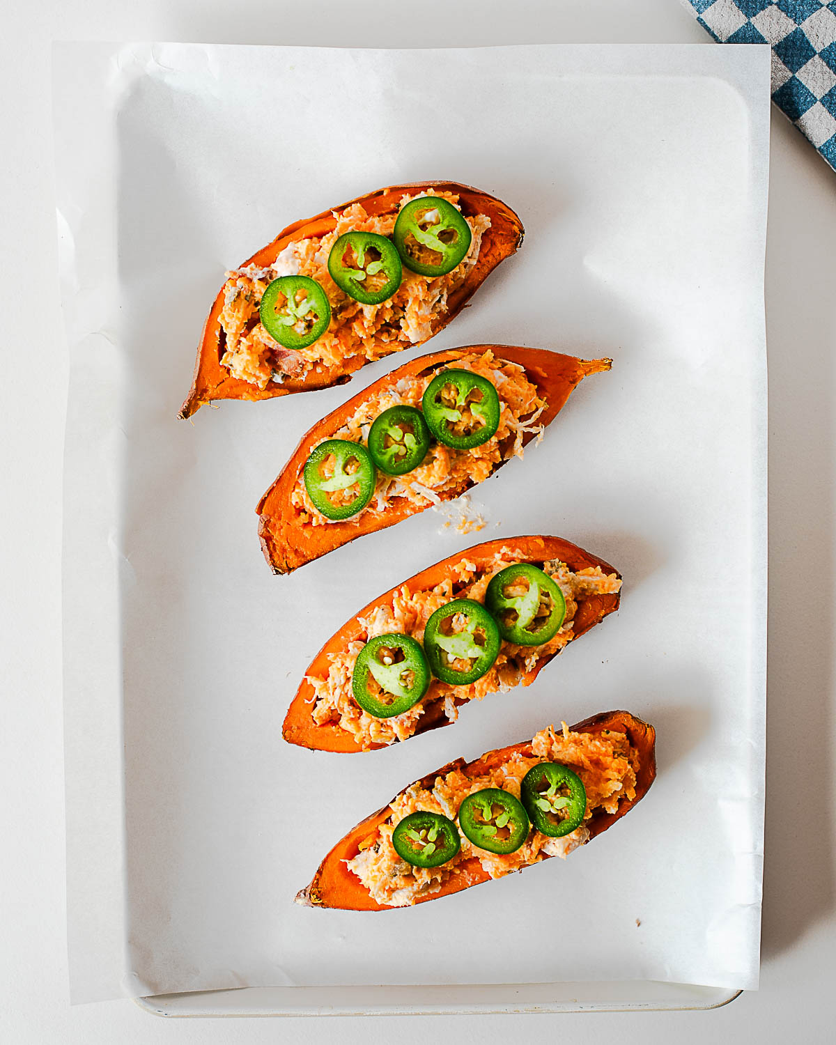 Stuffed sweet potato skins topped with sliced jalapeños before baking