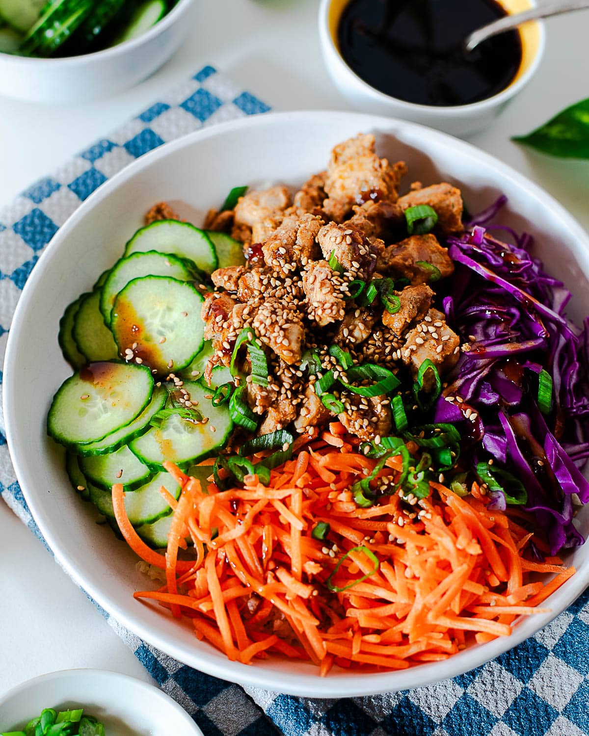High protein Korean BBQ chicken bowl with cucumbers, carrots, cabbage, and green onion.