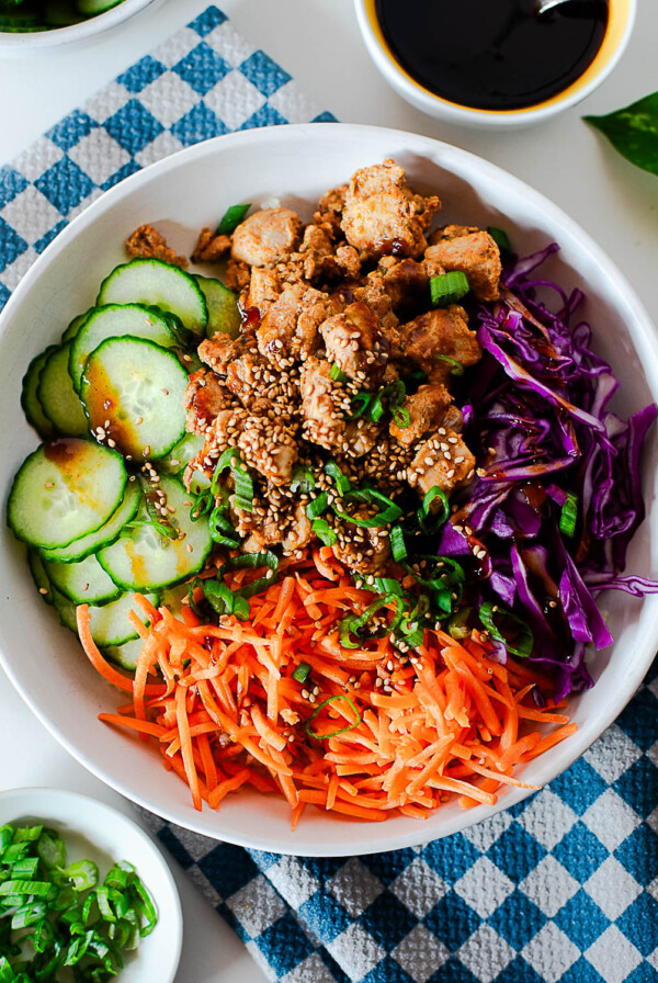 Korean BBQ chicken bowl with cauliflower rice, cucumbers, shredded carrots, purple cabbage, green onion, and sesame seeds.