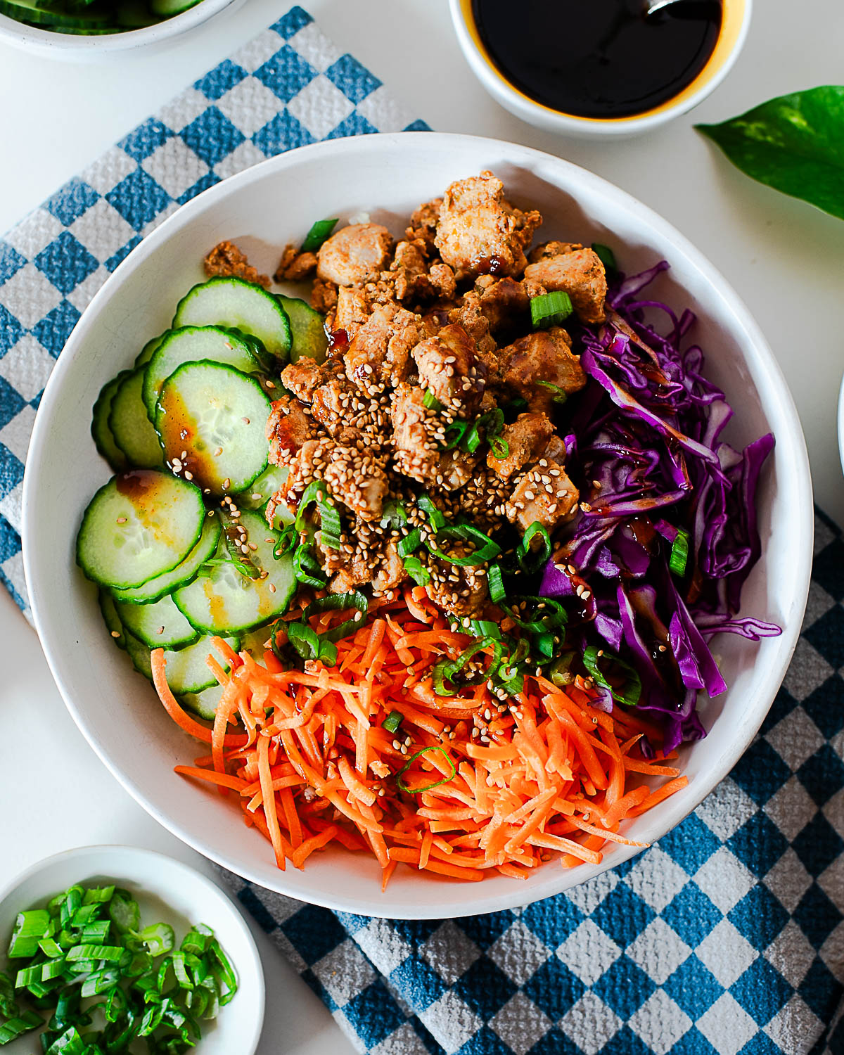 Korean BBQ chicken bowl with cauliflower rice, cucumbers, shredded carrots, purple cabbage, green onion, and sesame seeds.