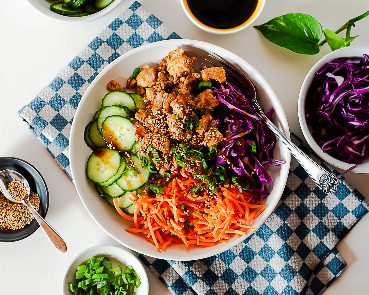 Colorful Korean BBQ chicken rice bowl topped with sesame seeds and fresh vegetables.