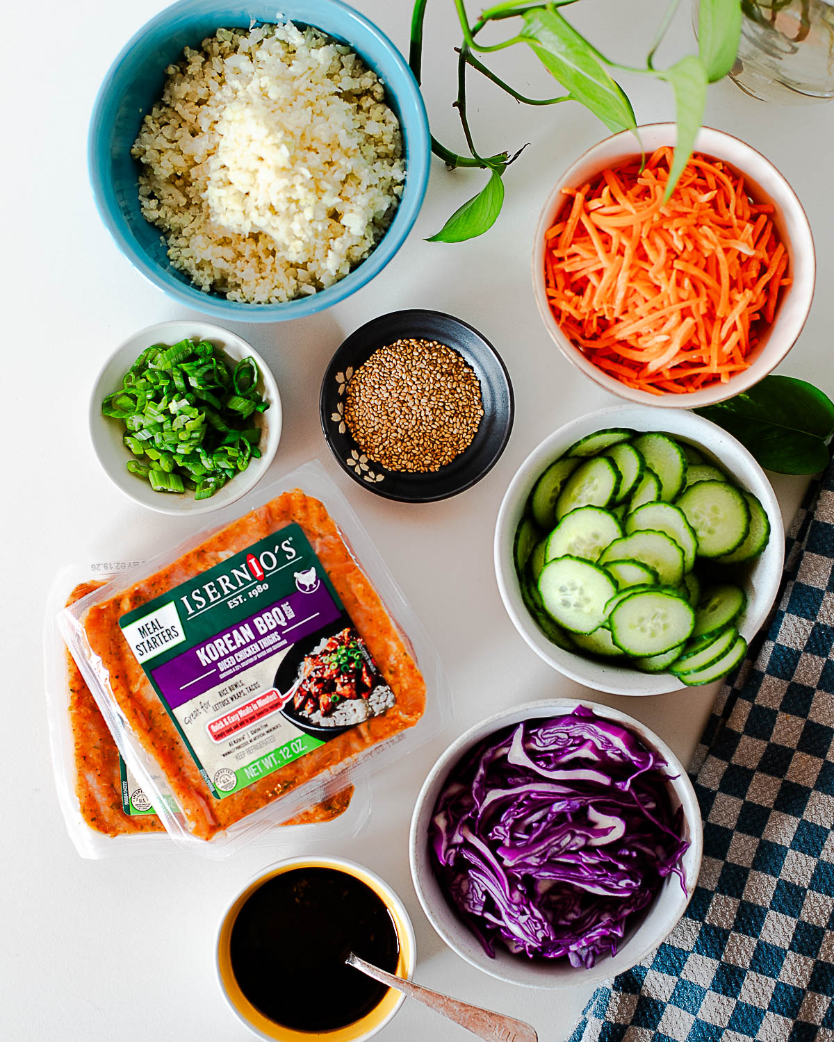 Ingredients for Korean BBQ chicken bowls including cauliflower rice, shredded carrots, cucumber, cabbage, sesame seeds, and Korean BBQ chicken.