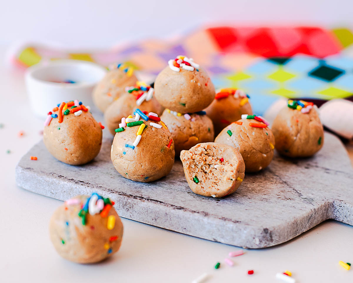 Rolled birthday cake protein balls on a marble board with rainbow sprinkles on top.