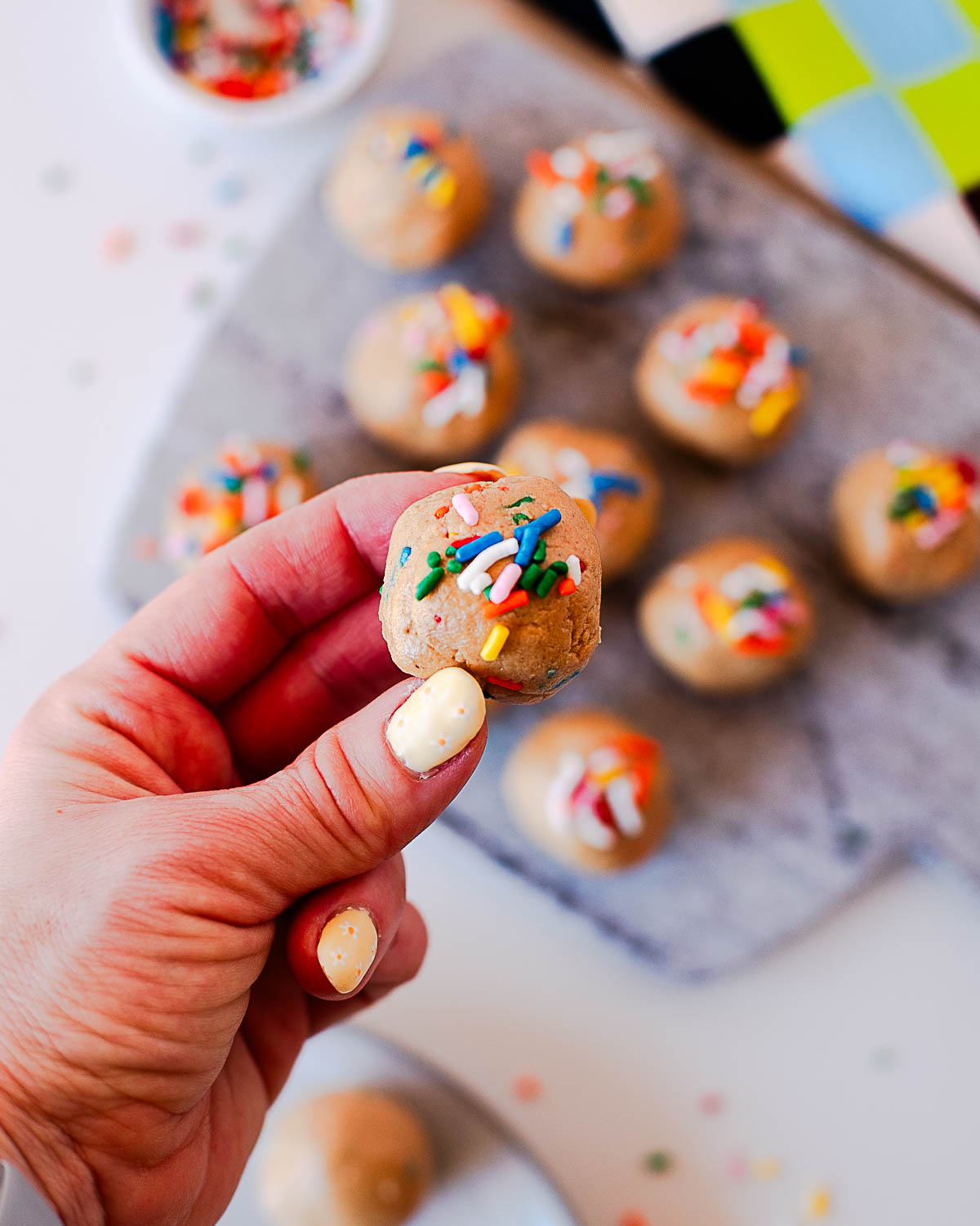 Hand holding a single birthday cake protein ball with sprinkles, soft texture visible.