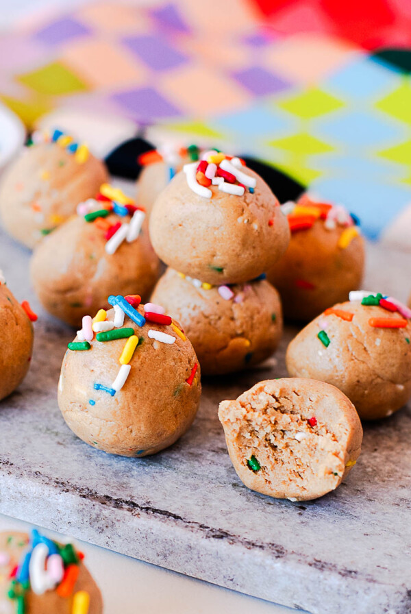 Close-up of birthday cake protein balls stacked with a bite showing the inside texture.