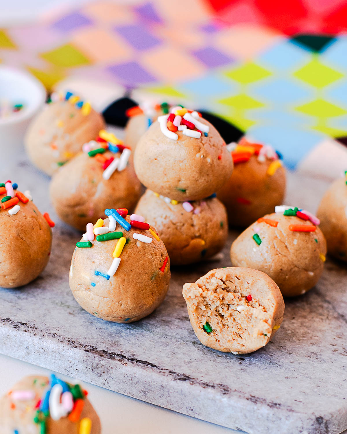 Close-up of birthday cake protein balls stacked with a bite showing the inside texture.