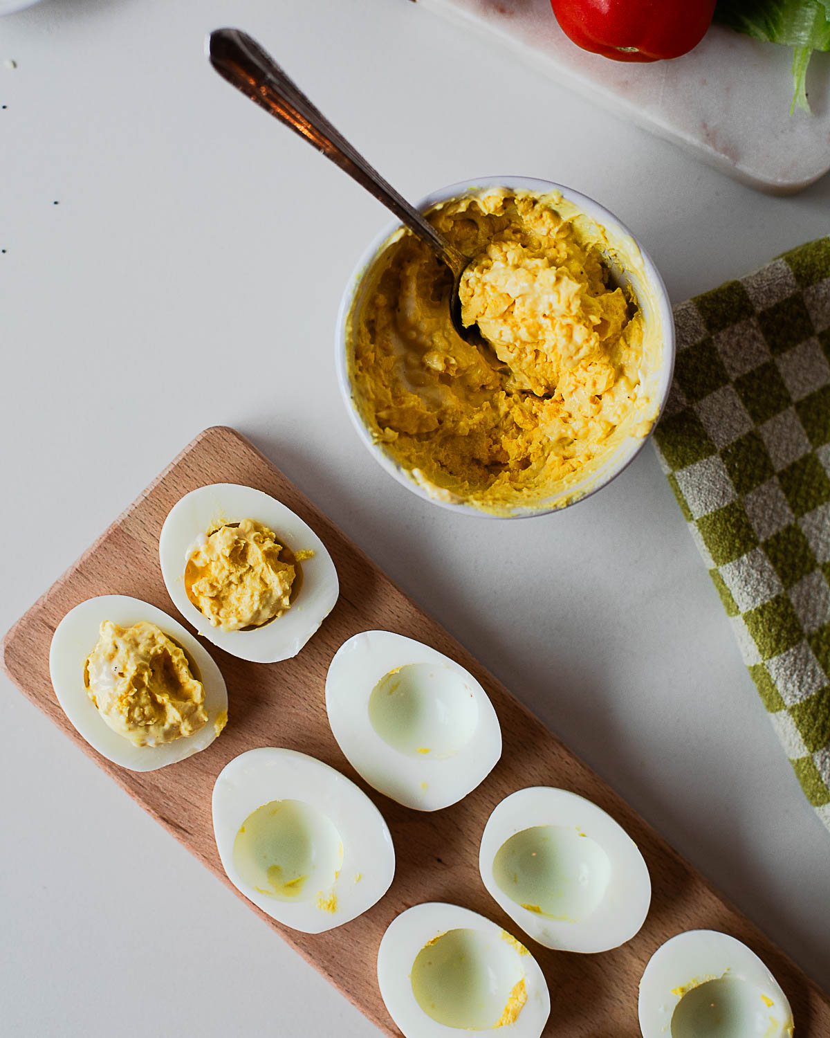 Deviled egg filling spooned into egg whites on a wooden board with extra filling in a bowl
