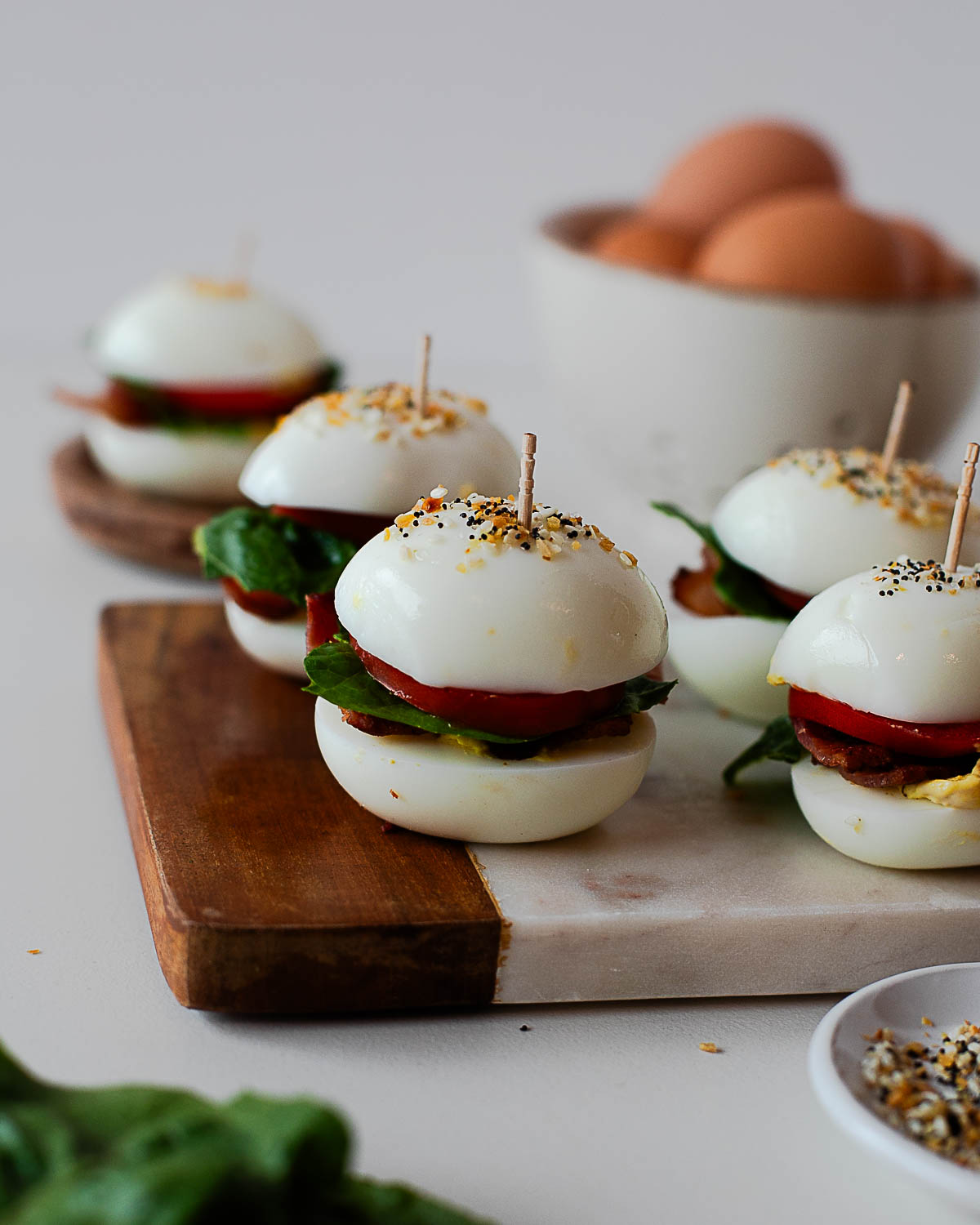 Close-up of a BLT deviled egg slider with crispy bacon, fresh lettuce, and tomato on a wooden plate