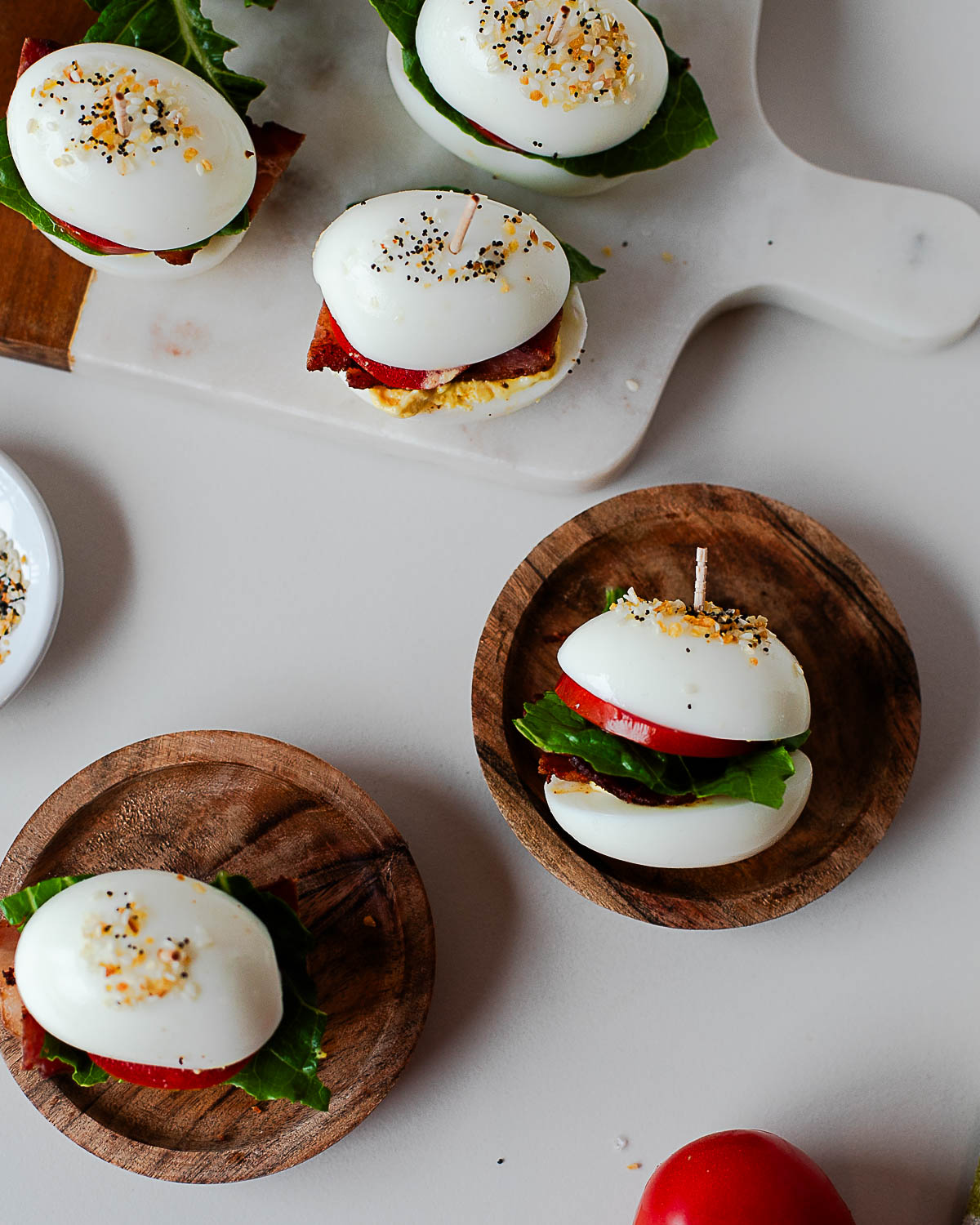 Overhead view of BLT deviled egg sliders on small plates with everything bagel seasoning