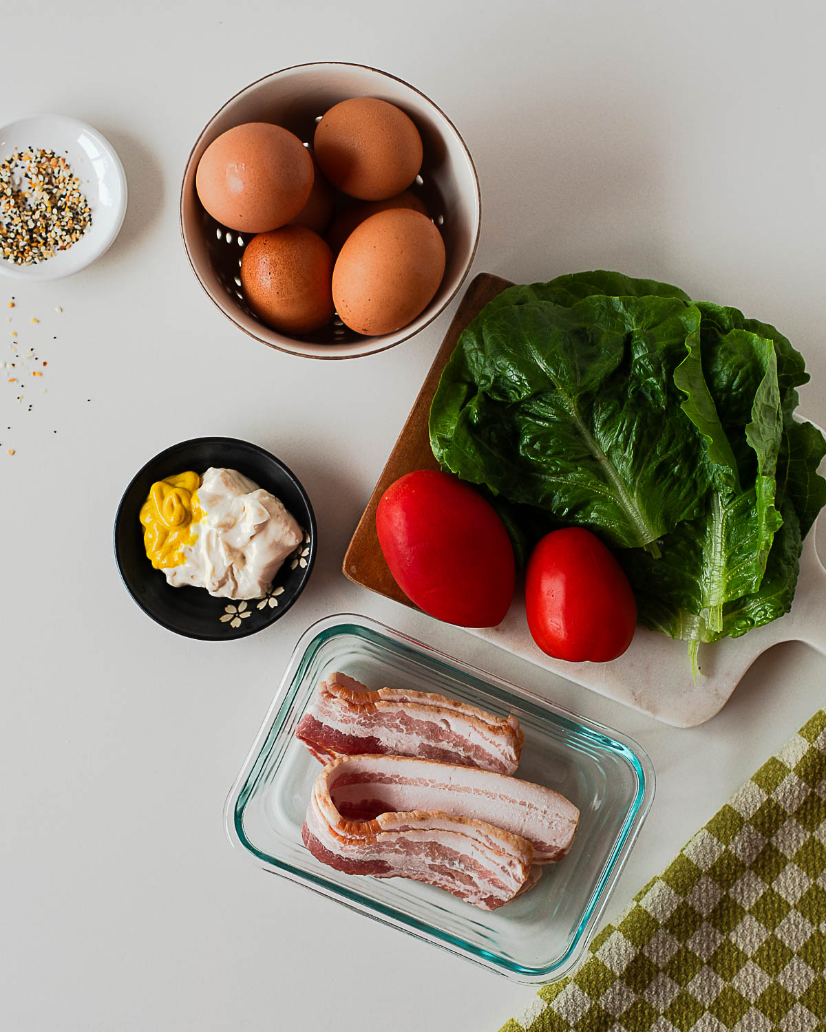 Ingredients for BLT deviled eggs including eggs, bacon, lettuce, tomato, mayo, and mustard on a cutting board