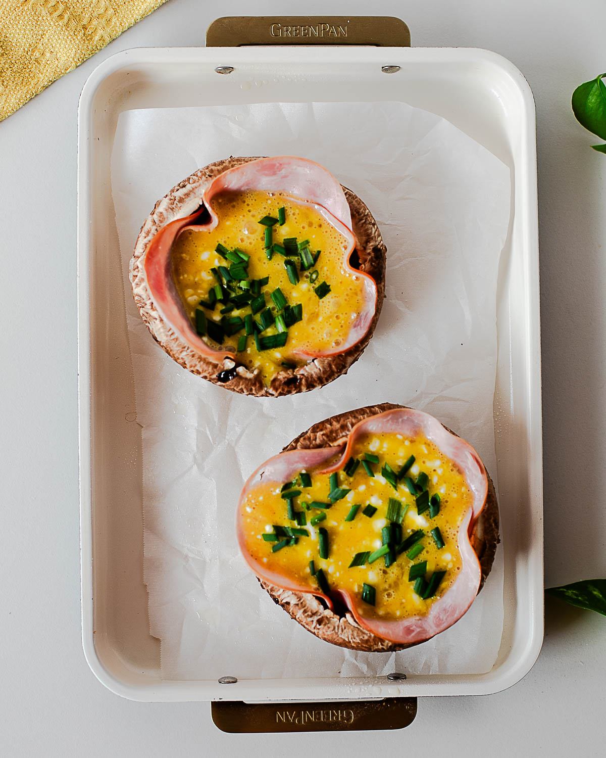 Portobello mushrooms stuffed with ham, eggs, and chives before baking on a parchment-lined baking sheet