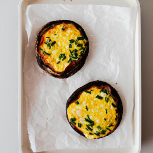 Overhead view of baked egg stuffed portobello mushroom caps with golden tops and herbs