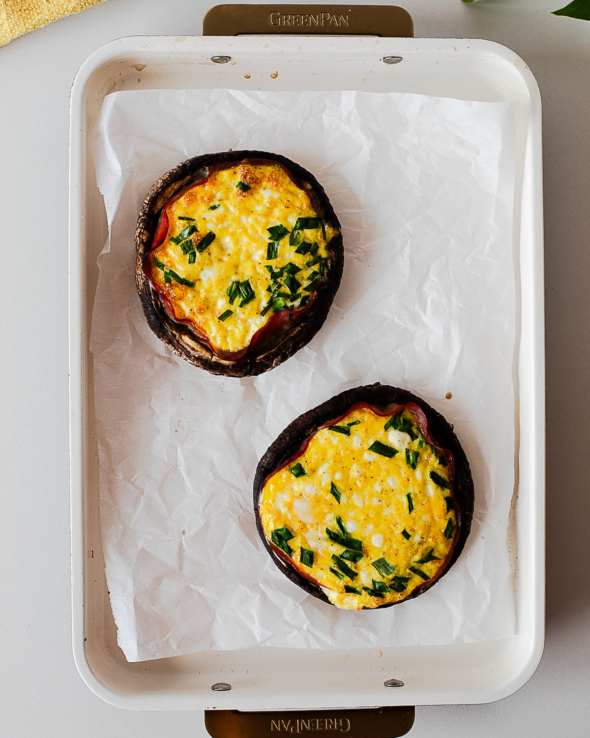 Overhead view of baked egg stuffed portobello mushroom caps with golden tops and herbs