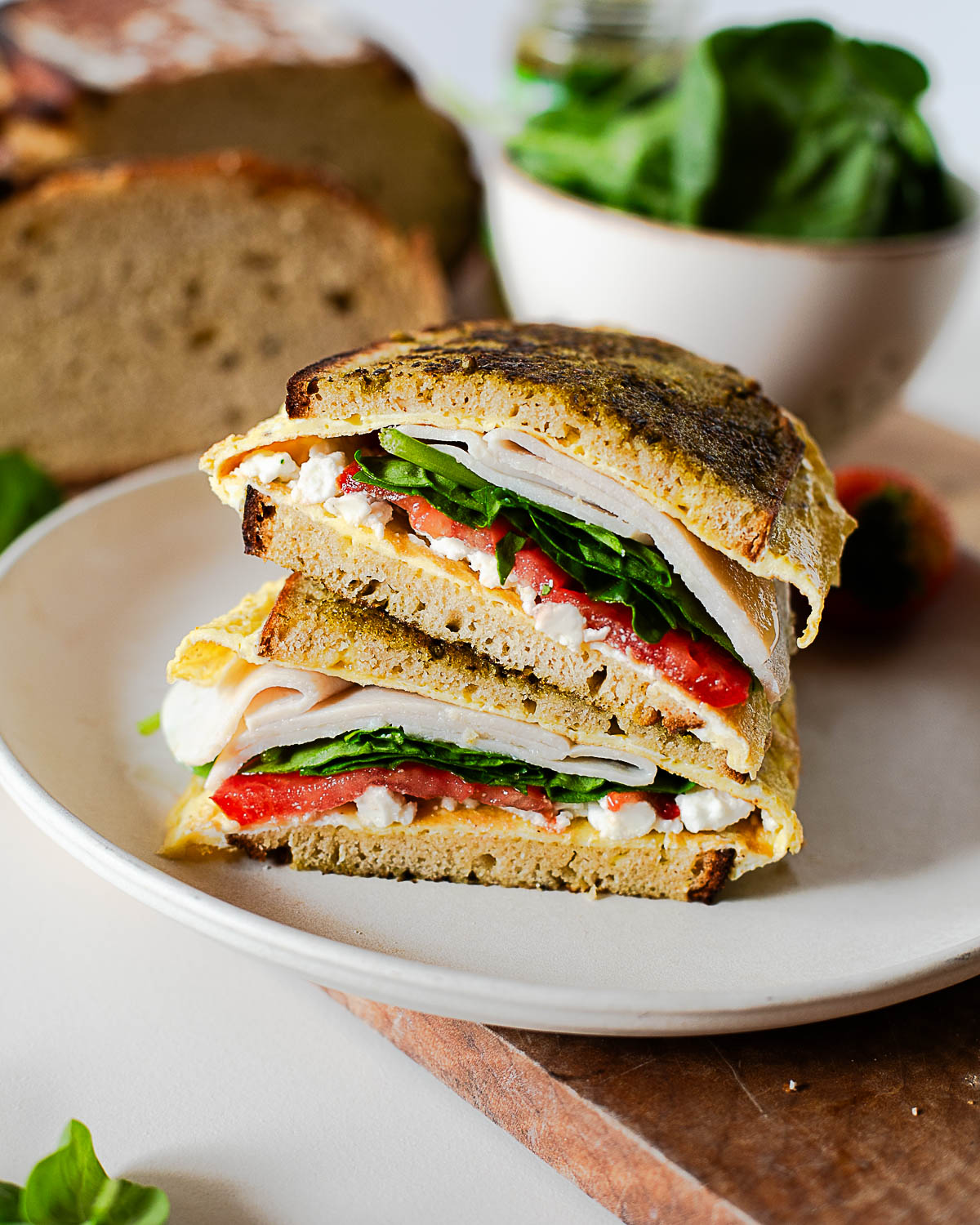 High protein pesto egg breakfast sandwich cut in half with turkey, spinach, tomato, and feta on crispy golden brown bread