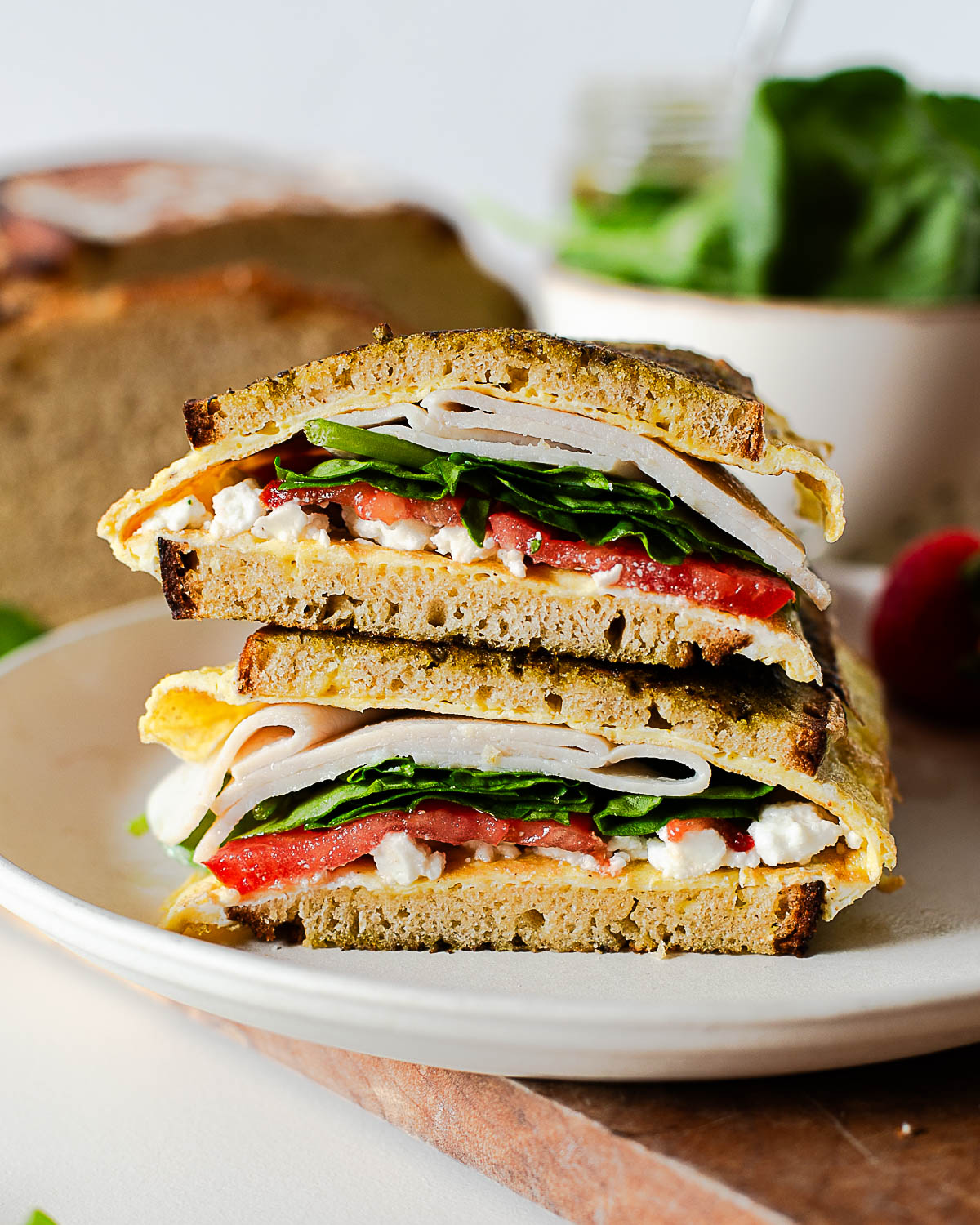 Pesto breakfast sandwich with eggs, feta, turkey, spinach, and tomato on toasted einkorn bread, sliced and stacked on a plate