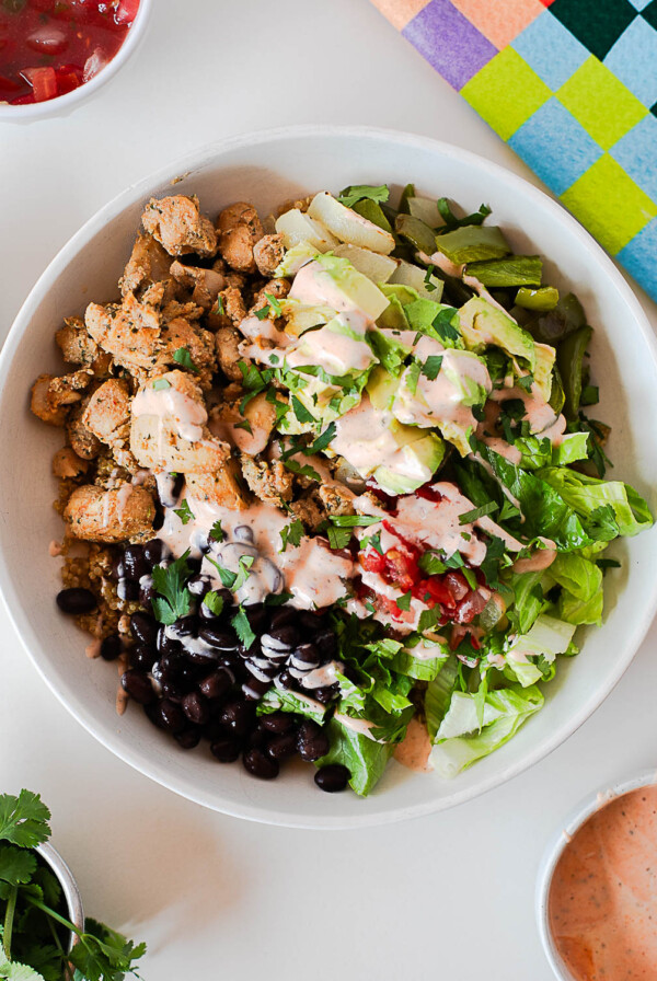 Southwest chicken burrito bowl with quinoa, black beans, avocado, lettuce, pico de gallo, and creamy spicy ranch drizzle.