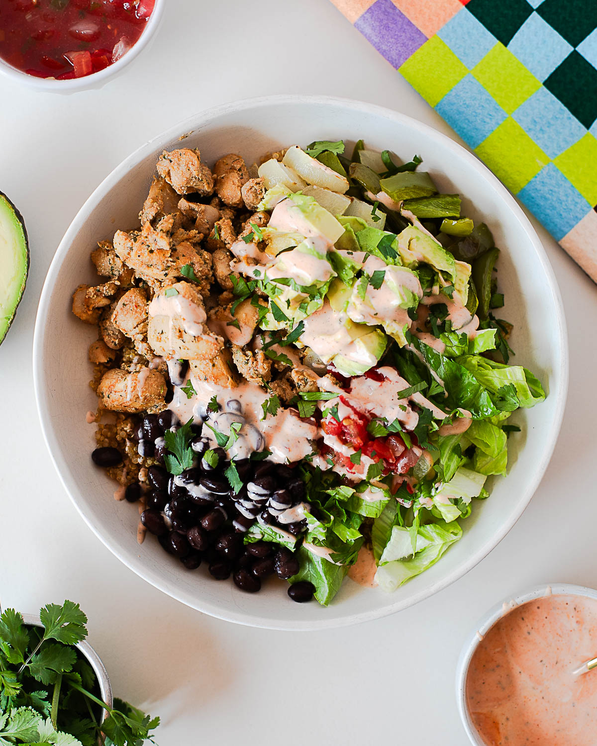 Southwest chicken burrito bowl with quinoa, black beans, avocado, lettuce, pico de gallo, and creamy spicy ranch drizzle.