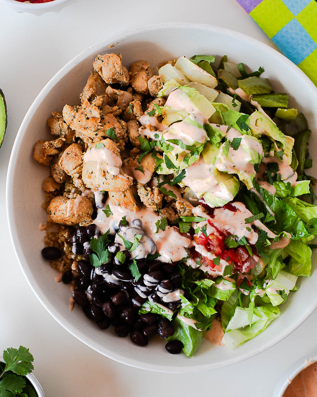 High-protein burrito bowl with chicken, black beans, quinoa, avocado, lettuce, and a creamy spicy dressing.