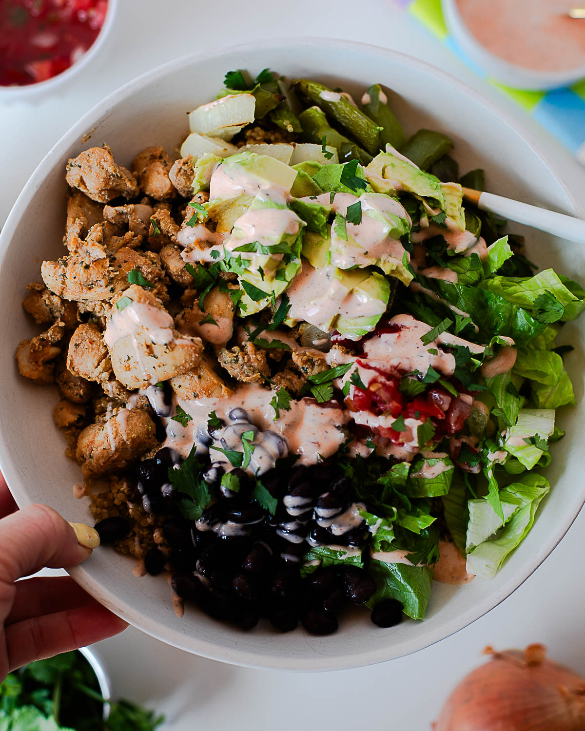 Hand holding a southwest chicken burrito bowl filled with quinoa, chicken, black beans, avocado, and fresh greens.