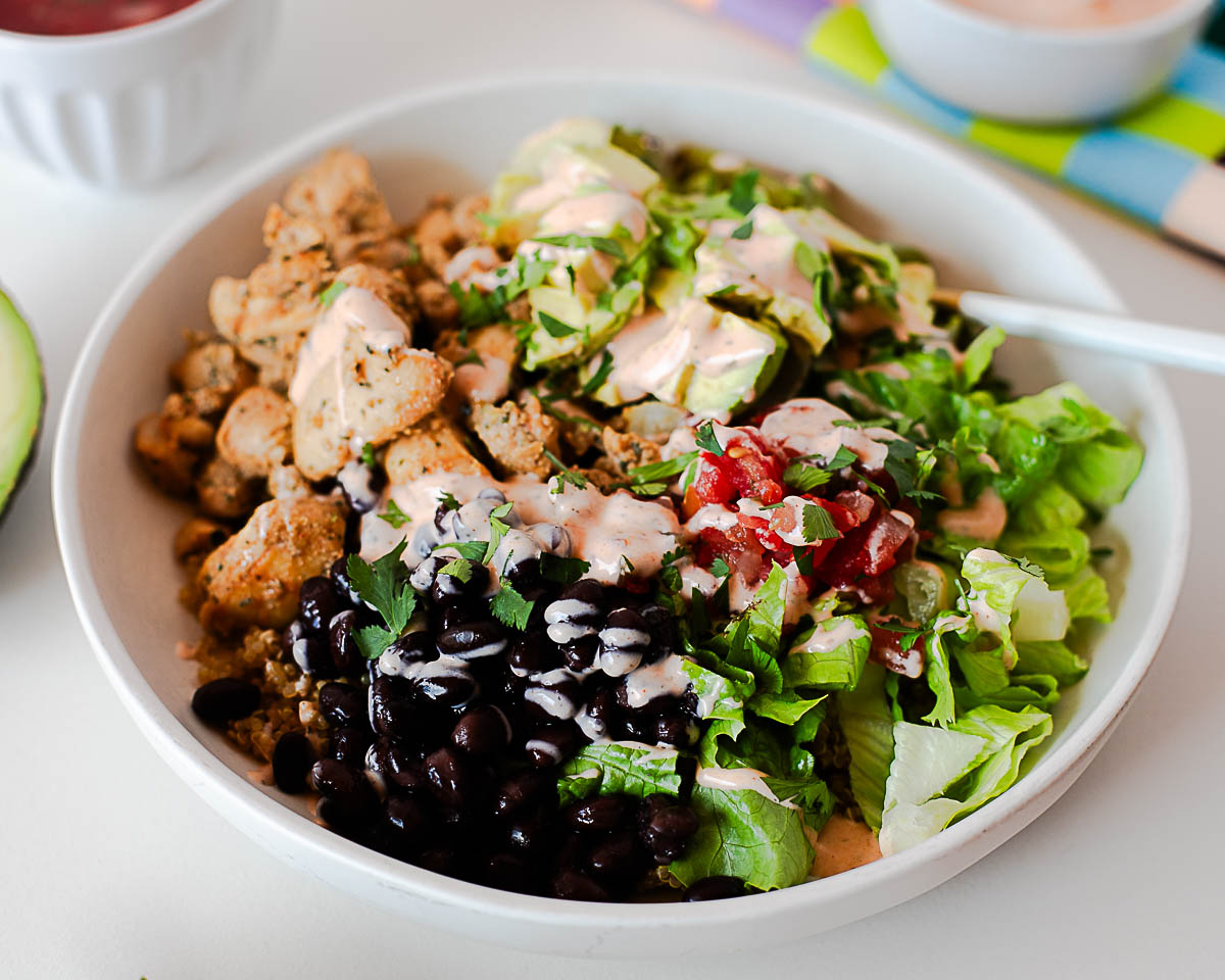 Close-up of a high-protein southwest chicken burrito bowl with chicken, quinoa, black beans, avocado, and fresh toppings.