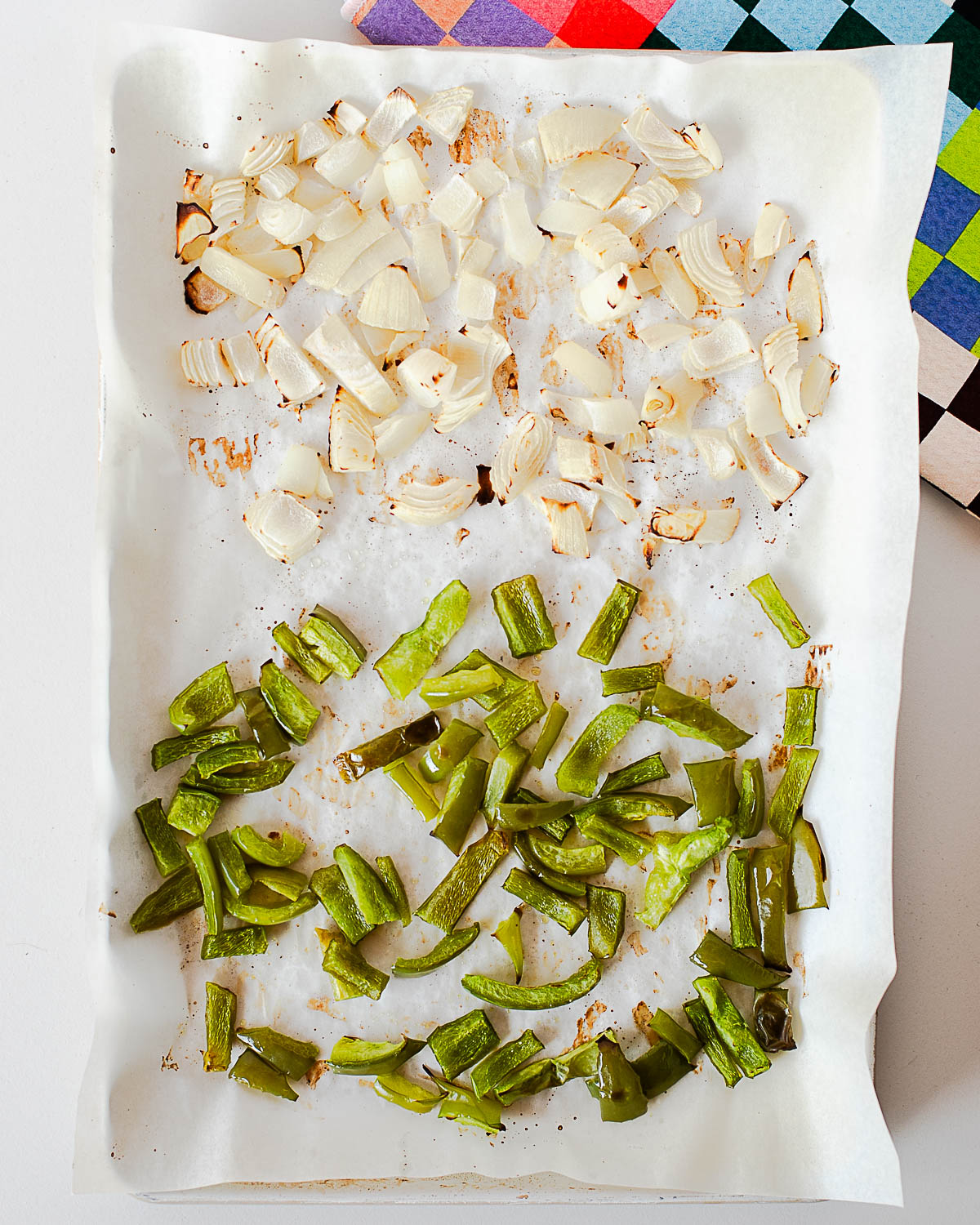 Roasted bell peppers and onions on a parchment-lined baking sheet, lightly caramelized and ready for burrito bowls.