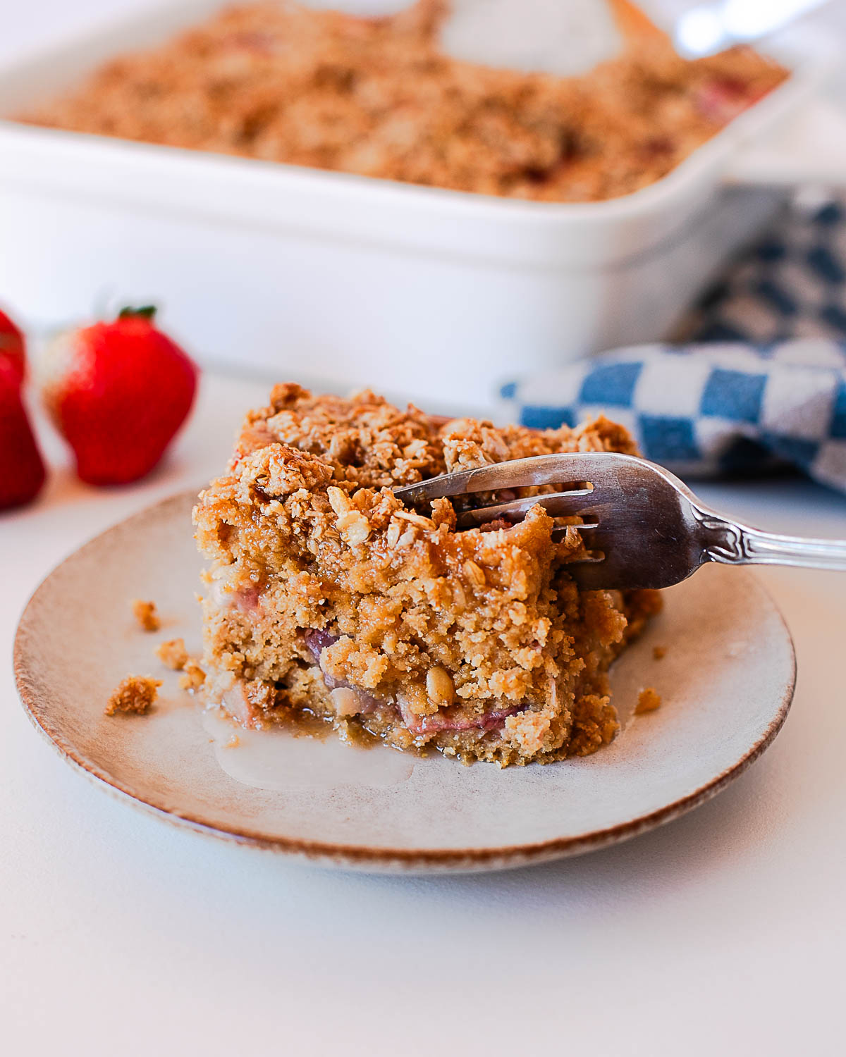 Fork cutting into soft strawberry crumb coffee cake slice with crumble topping